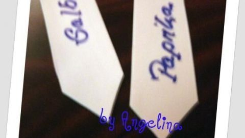 Zwei weiße Beetstecker mit blauen Beschriftungen "Salbei" und "Paprika" liegen auf dunklem Holz. Text: "by Angelina".