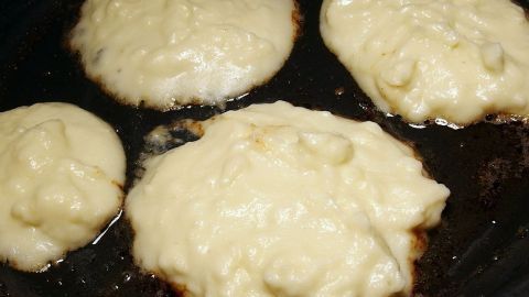 Knusprige Küchlein aus Kartoffelpüree braten in einer Pfanne, goldbraun und appetitlich, umgeben von dampfender Hitze.