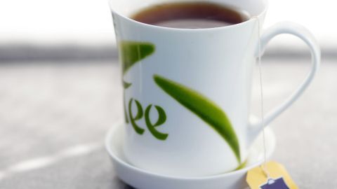 Eine Tasse mit schwarzem Tee steht auf einer Untertasse, mit einem Teebeutel, auf einer hellen Oberfläche.