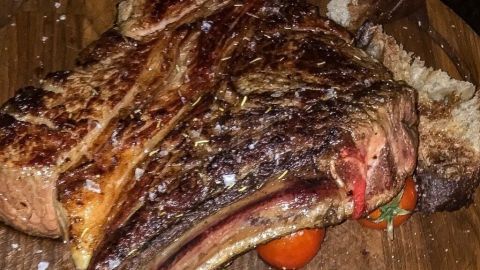 Ein saftiges Steak liegt auf einem Holzbrett, neben gebratenem Gemüse und frischen Tomaten, bereit zum Servieren.
