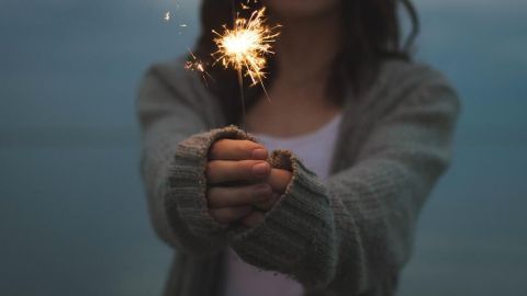 Eine Person hält eine Wunderkerze in die Kamera, umgeben von einer stimmungsvollen, leicht verschwommenen Landschaft, die Vorfreude auf Silvester vermittelt.