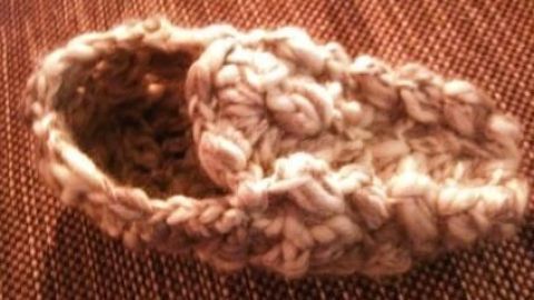 Ein Hüttenschuh aus dickem Garn liegt auf einem strukturierten Untergrund und zeigt die handgefertigte Häkelarbeit.