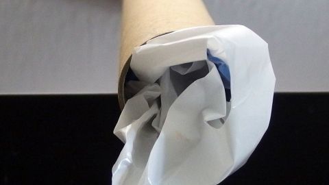 Eine Papprolle enthält gefaltete Plastiktüten, die ordentlich verstaut sind, auf einem schlichten Tisch in einem Raum.