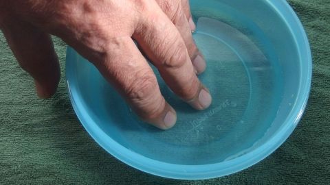 Eine Hand taucht in eine Schüssel mit Wasser, um die Entzündung an den Nagelbetten zu behandeln.