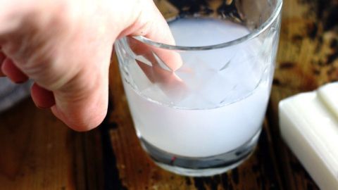 Ein Hand hält eine Glas mit milchiger Flüssigkeit, während sie zur Behandlung des entzündeten Nagelbettes in der Küche verwendet wird.