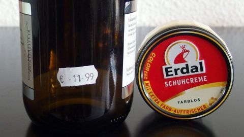 Ein Glasbehälter mit einem Preisaufkleber und einer Dose Erdal Schuhcreme stehen auf einem schwarzen Tisch.