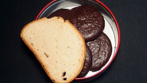 Ein Stück Brot liegt neben einer Auswahl an Plätzchen in einer roten Dose auf schwarzem Hintergrund.