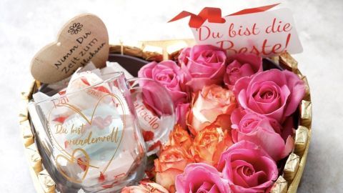 Ein herzförmiger Geschenkkorb mit rosa Rosen, einer Tasse und Süßigkeiten zeigt eine liebevolle Dankesbotschaft.