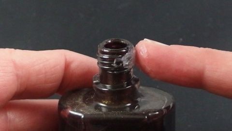 Mit Vaseline verklebt das Gewinde eines Nagellackfläschchens nicht und lässt sich immer gut öffnen. Ein Nagellackfläschchen wird mit einem Finger berührt, um es zu öffnen, während es auf einem dunklen Untergrund steht.