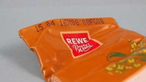 Eine geöffnete Tube mit dem Haltbarkeitsdatum "15.04.15" ist auf einer hellen Oberfläche platziert, das Logo von REWE ist sichtbar.