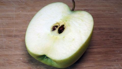 Ein geschnittenem grüner Apfel liegt auf einem Holzbrett und zeigt seine frische, saftige Innenseite mit Kernen.