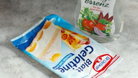 Essigflasche und Gelatinepackung liegen auf einer hellen Oberfläche, bereit zur Anwendung gegen Abflussprobleme.