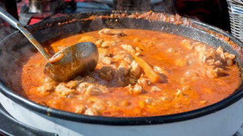 Ein großer Pfundstopf kocht dampfend in einem Topf, während ein Löffel Rühren im würzigen Eintopf aus Fleisch und Gemüse.
