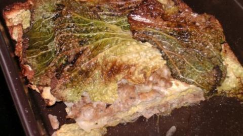 Eine flachgelegte Kohlroulade liegt in einer Backform, leicht anger&ouml;stet, umgeben von einer goldbraunen Kruste.