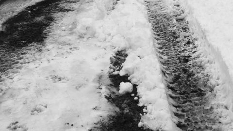 Schnee und Streusalz liegen auf einer Straße, während Reifenspuren durch das Salz hindurchführen.