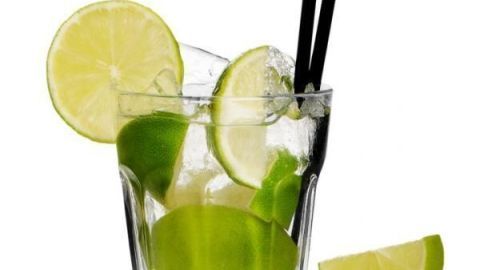 Ein Glas Mojito mit Limettenscheiben und Eiswürfeln auf weißem Hintergrund, zwei schwarze Strohhalme ragen heraus.