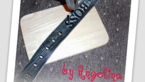 Ein Gürtel wird auf einem Holzbrett bearbeitet, während ein Hammer darauf schlägt, um ein neues Loch zu schaffen.