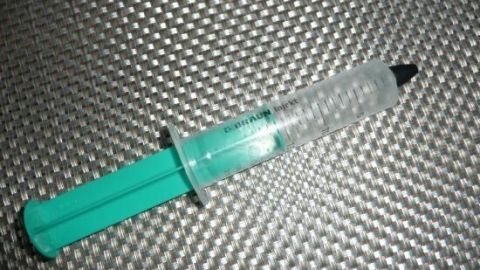 Eine grüne Spritze liegt auf einer silbernen, strukturierten Oberfläche. Text: "B. BRAUN INJECT".