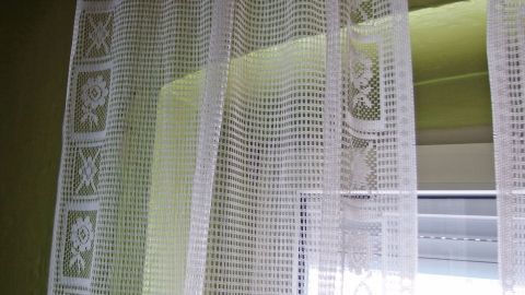 Weiße Gardinen hängen vor einem Fenster, leicht im Licht wehend, umgeben von einem hellgrünen Raum.