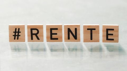Holzbuchstaben bilden das Wort "#RENTE" auf einer spiegelnden Oberfläche, ausgestattet für ein Thema zur Rente.