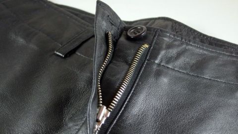 Ein kaputter Reißverschluss an Lederhosen liegt offen da, während man versucht, ihn zu reparieren, um Kosten zu sparen.