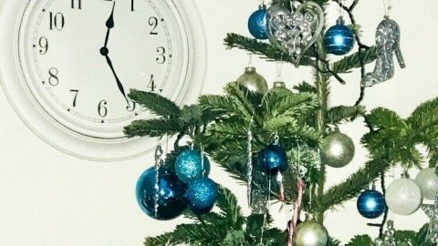 Der Weihnachtsbaum mit blauen Kugeln und einem glänzenden Stern steht im Raum, während eine Uhr die Zeit anzeigt.