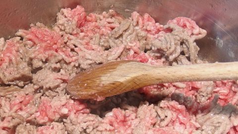 Hackfleisch wird mit einem Holzlöffel in einem Topf angebraten, um eine Bolognesesoße zuzubereiten.