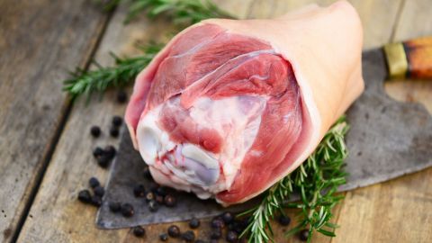 Ein Schweinefleischstück liegt auf einem Brett, umgeben von Kräutern und Pfefferkörnern, bereit zum Pökeln.