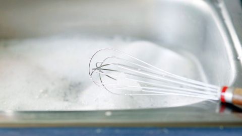 Eine Quirlschüssel bewegt sich in einem Spülbecken voller Seifenwasser, während Geschirrspülen stattfindet.