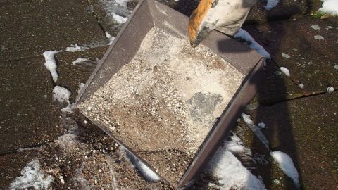 Ein Schaufel bewegt sich, um Asche auf einer glatten, rutschigen Fläche zu verteilen, während einige Schneereste sichtbar sind.