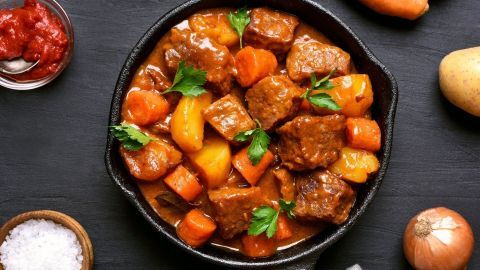 Ein köstlicher Möhreneintopf mit Rindfleisch und frischem Gemüse wird in einer gusseisernen Pfanne serviert, umgeben von Kartoffeln und Zutaten.