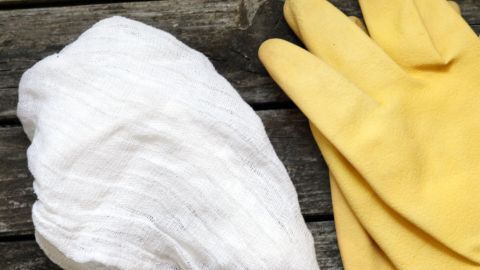 Ein fusselfreies Tuch liegt neben gelben Gummihandschuhen auf einer rustikalen Holzoberfläche, ideal für Reinigungsarbeiten.