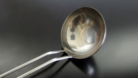 Ein Metallbecher mit langen Griffen liegt auf einem schwarzen Untergrund, bereit zur Urinprobe vom Hund für den Tierarzt.
