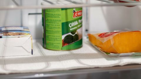 Im Kühlschrank liegt Küchenpapier auf dem Regal, während eine Dose und ein Stück Käse darauf platziert sind.