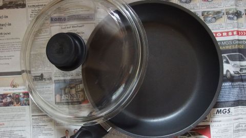 Eine Pfanne mit Deckel liegt auf Zeitungsblättern, ideal zum Füttern von Katzen mit Nassfutter und für einfache Reinigung.