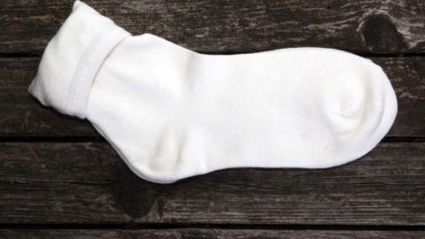 Eine weiße Socke liegt auf einer dunklen Holzoberfläche und wartet darauf, gewaschen und ohne Sortierung verwendet zu werden.