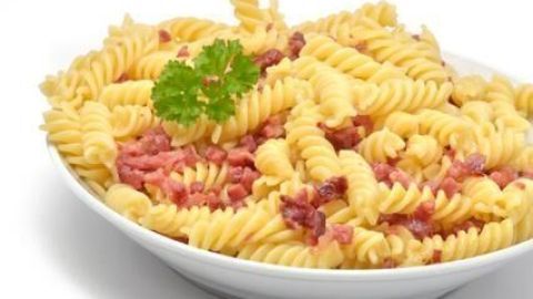 Eine weiße Schüssel mit Schinkennudeln, garniert mit einem Petersilienzweig, steht vor einem weißen Hintergrund.