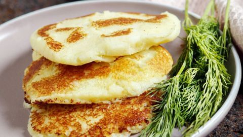 Drei goldbraune Kartoffelplätzchen liegen auf einem Tellern, umgeben von frischen Kräutern, auf einer rustikalen Oberfläche.