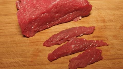 Rohes Fleisch liegt auf einem Holzbrett, fein geschnittene Stücke neben einem größeren Stück, bereit zum Einfrieren.