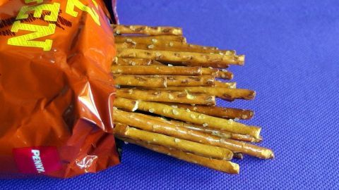 Knusprige Salzstangen liegen aus einer offenen Tüte auf einer blauen Unterlage, bereit zum Essen gegen Sodbrennen.