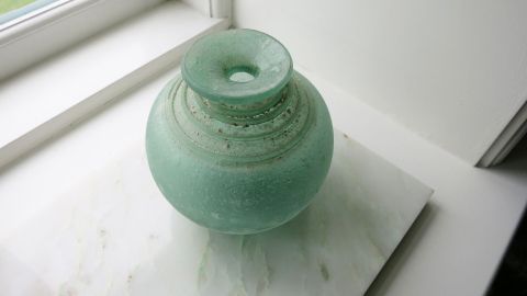 Mit einer Mischung aus Essigessenz und Salz, festsitzenden Schmutz an unzugänglichen Vasenböden lösen. Eine grünliche Glasblumen vase steht auf einem weißen Tisch in der Nähe eines Fensters, lichtdurchflutet und sauber.
