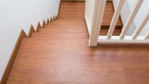 Laminatboden glänzt streifenfrei auf Treppe neben weißem Geländer in modernem Treppenhaus mit heller Wand.