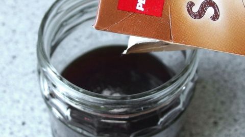 Ein Glas mit dunkler Flüssigkeit wird von einem Karton mit der Aufschrift "Sahne" übergossen. Die Küchensituation deutet auf Kochaktivität hin.