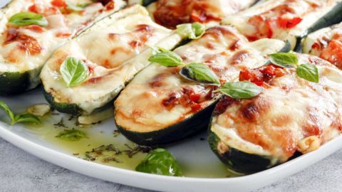 Überbackene Zucchini auf einem weißen Teller, mit geschmolzenem Käse und frischen Kräutern, appetitlich angerichtet.