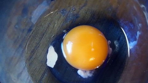 Ein Eigelb liegt in einer Schüssel, umgeben von klarem Eiweiß, auf einer Holzoberfläche.