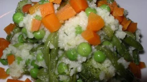 Couscous mit grünem Gemüse und Karottenwürfeln wird appetitlich auf einem Teller serviert, umgeben von frischer Kräutersauce.