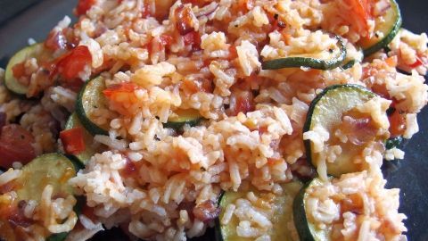 Bunter Gemüsereis liegt auf einem schwarzen Teller, während er appetitlich angerichtet und mit frischem Gemüse verfeinert ist.