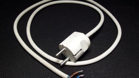 Ein elektrischer Stecker liegt auf einem dunklen Untergrund und ist mit einem weißen Kabel verbunden, das unbenutzt ist.