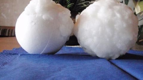Zwei weiße Schneebälle aus Wachs liegen auf einem blauen Tuch, dekorativ zwischen Pflanzen im Hintergrund platziert.