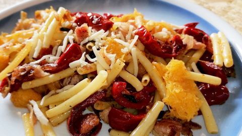 Eine bunte Spaghetti-Kürbis-Pfanne mit Röstaromen ist auf einem Teller angerichtet, umgeben von einer hellen Tischoberfläche.
